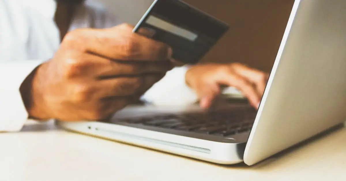 person holding their credit card out in front of their laptop