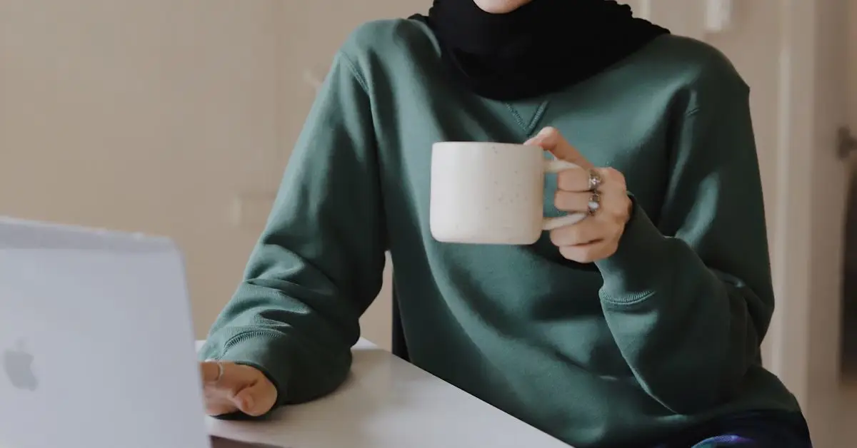 person holding a coffee mug sitting in front of a laptop